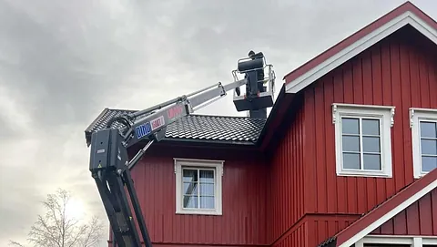 Arbeid fra lift på taket av rødt trehus