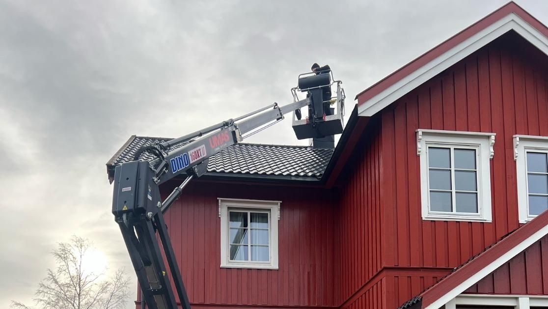 Arbeid fra lift på taket av rødt trehus